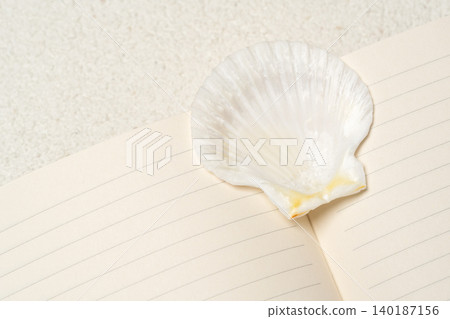 Elegant flat lay scene featuring a large white scallop seashell resting on open lined notebook. Elegant flat lay scene featuring a large white scallop seashell resting on open lined notebook. 140187156