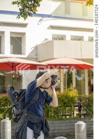 Side view of a Indonesian southeast asian male traveler with a backpack capturing a picture with his digital camera on an urban street near a historic building. Travel or vacation concept Side view of a Indonesian southeast asian male traveler with a backpack capturing a picture with his digital camera on an urban street near a historic building. Travel or vacation concept 140187324