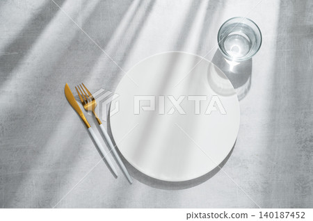 An empty white plate with glass of water, fork, knife on a gray concrete background An empty white plate with glass of water, fork, knife on a gray concrete background 140187452