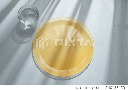 An empty yellow plate with glass of water on a blue background with sunlight. An empty yellow plate with glass of water on a blue background with sunlight. 140187453