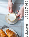 Hand holding a cup of cappuccino coffee on a blue tile background with fresh croissants 140187469