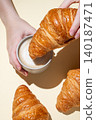 Hands holding a cup of cappuccino coffee and croissant on a yellow isolated background 140187471