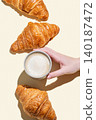 Hand holding a cup of cappuccino coffee on a yellow isolated background with fresh croissants 140187472