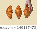 Hand holding a croissant on a yellow isolated background with fresh pastry and shadow 140187473