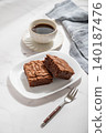 A pieces of chocolate brownie on a plate and a cup of espresso coffee on a light marble background 140187476