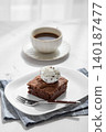 A piece of chocolate brownie with ice cream on a plate and a cup of espresso coffee 140187477