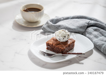 A piece of chocolate brownie with ice cream on a plate and a cup of espresso coffee 140187479
