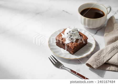 A piece of chocolate brownie with ice cream on a plate and a cup of espresso coffee A piece of chocolate brownie with ice cream on a plate and a cup of espresso coffee 140187484