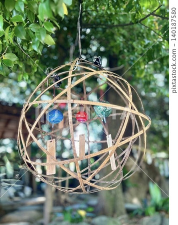 Colorful Edo-style wind chimes in three different colors hang in a bamboo basket, shining brightly in the dappled sunlight filtering through the trees. Colorful Edo-style wind chimes in three different colors hang in a bamboo basket, shining brightly in the dappled sunlight filtering through the trees. 140187580