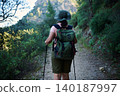Woman hiking on forest trail with backpack and trekking poles during outdoor adventure 140187997
