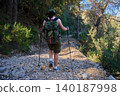 Woman hiking on rocky forest trail with backpack and trekking poles at golden hour 140187998
