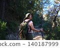Woman hiker with backpack and walking pole on a forest trail looking back during an outdoor hike 140187999
