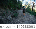 Woman hiking on forest trail with backpack and trekking poles 140188001