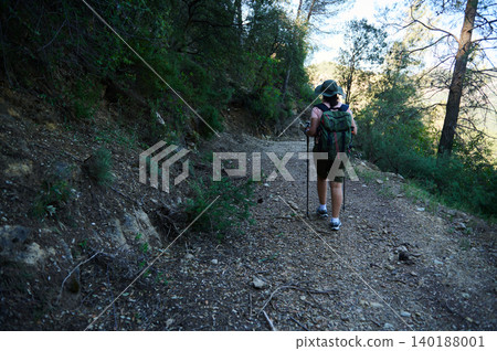 Woman hiking on forest trail with backpack and trekking poles Woman hiking on forest trail with backpack and trekking poles 140188001