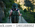 Woman hiking on a forest trail with backpack and trekking poles at golden hour 140188002