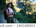 Woman hiking with trekking poles and backpack enjoying nature on a forest trail at sunrise 140188003