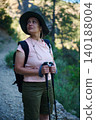 Woman hiking with backpack and trekking poles on a forest trail 140188004