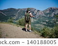 Woman hiking with backpack and poles overlooking terraced mountains and valley 140188005