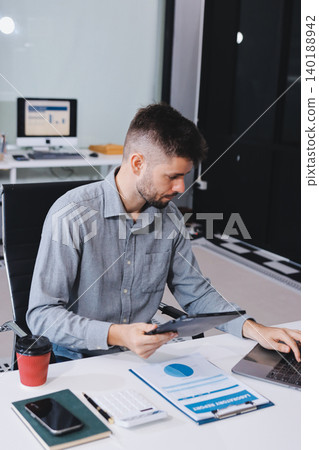 Tired worker. A tired businessman works in the evening. A man in office clothes is holding his temples. Problems in business. The businessman is trying to solve the problems that have arisen. 140188942