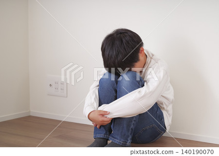 A little boy huddled against the wall, hugging his knees. A little boy huddled against the wall, hugging his knees. 140190070