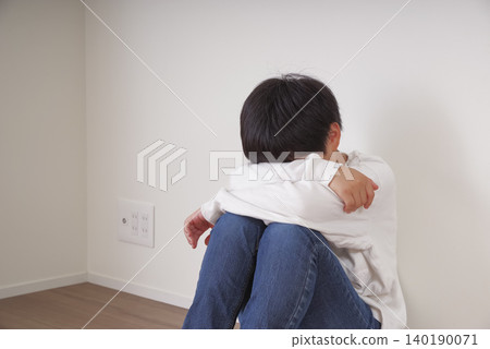 A little boy huddled against the wall, hugging his knees. A little boy huddled against the wall, hugging his knees. 140190071