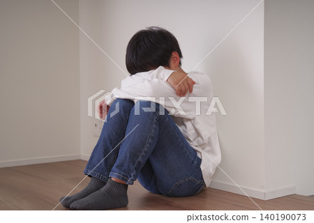 一個小男孩蜷縮在牆邊,抱著膝蓋。 一個小男孩蜷縮在牆邊,抱著膝蓋。 140190073