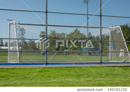 Green soccer Field and football goals Behind Chain Link Fence on a stadium. An empty outdoor football pitch with green artificial turf, white markings, a goalpost, and enclosed by high netting Green soccer Field and football goals Behind Chain Link Fence on a stadium. An empty outdoor football pitch with green artificial turf, white markings, a goalpost, and enclosed by high netting 140191230