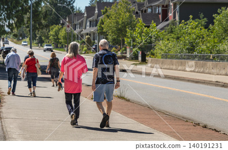 Old couple strolling on a leisurely urban walk on a sunny summer day. Senior people walking through a peaceful pedestrian street surrounded by greenery. Active aging concept. Old couple strolling on a leisurely urban walk on a sunny summer day. Senior people walking through a peaceful pedestrian street surrounded by greenery. Active aging concept. 140191231