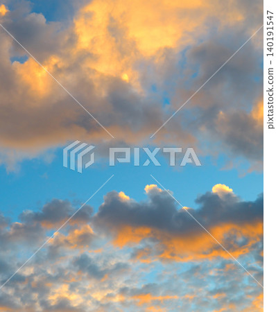 Premium vertical view of a beautiful dramatic sky filled with thick sunset clouds illuminated by bright orange golden hour light against a calm blue background. Premium vertical view of a beautiful dramatic sky filled with thick sunset clouds illuminated by bright orange golden hour light against a calm blue background. 140191547