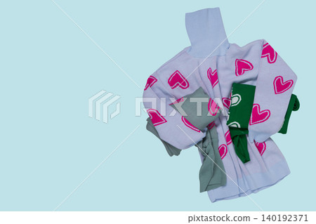 Creative concept of care and warmth with light blue knitted sweater hugging folded green and grey clothes on blue background, copy space. 140192371