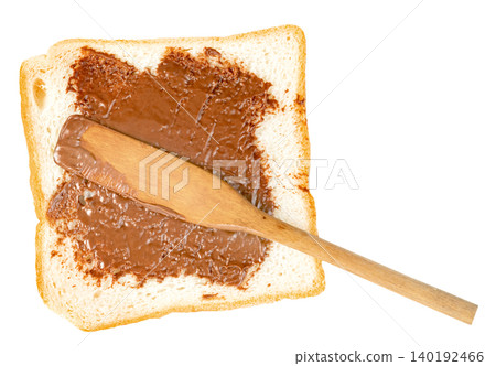 A slice of white toast bread with sweet chocolate hazelnut spread being applied with a wooden spatula. Top view of a delicious snack isolated. Perfect for food concepts. A slice of white toast bread with sweet chocolate hazelnut spread being applied with a wooden spatula. Top view of a delicious snack isolated. Perfect for food concepts. 140192466