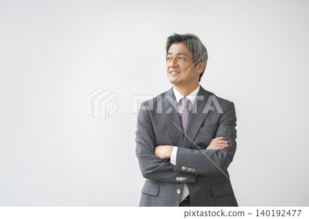 一位六十多歲的男子，身穿西裝，雙手交叉放在胸前，面帶微笑。 140192477