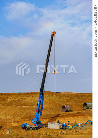 在建築工地和起重機作業區的上空,藍天中出現了一道淡淡的彩虹。 在建築工地和起重機作業區的上空,藍天中出現了一道淡淡的彩虹。 140192597