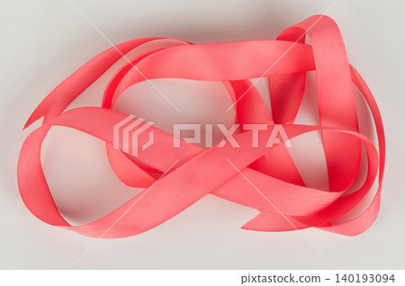 Colorful pink ribbon is placed on a plain surface 140193094