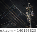 The silent silhouettes of utility poles and power lines stretching into the night sky. 140193823