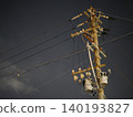 The silent silhouettes of utility poles and power lines stretching into the night sky. 140193827