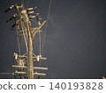 The silent silhouettes of utility poles and power lines stretching into the night sky. 140193828