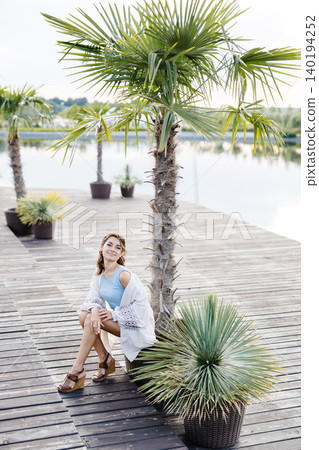 A Woman Relaxing Under a Palm Tree on a Secluded Dock, Surrounded by the Calming Sounds of the Water A Woman Relaxing Under a Palm Tree on a Secluded Dock, Surrounded by the Calming Sounds of the Water 140194252