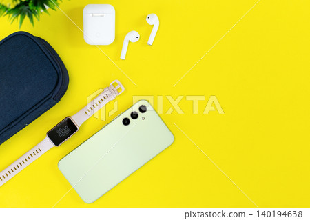 Minimalist tech setup on bright yellow background. Modern smartphone, smartwatch, earbuds, and case neatly arranged. Clean aesthetic suits lifestyle, wellness, or tech-focused content Minimalist tech setup on bright yellow background. Modern smartphone, smartwatch, earbuds, and case neatly arranged. Clean aesthetic suits lifestyle, wellness, or tech-focused content 140194638