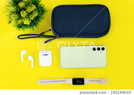 Minimalist tech setup on bright yellow background. Modern smartphone, smartwatch, earbuds, and case neatly arranged. Clean aesthetic suits lifestyle, wellness, or tech-focused content Minimalist tech setup on bright yellow background. Modern smartphone, smartwatch, earbuds, and case neatly arranged. Clean aesthetic suits lifestyle, wellness, or tech-focused content 140194639