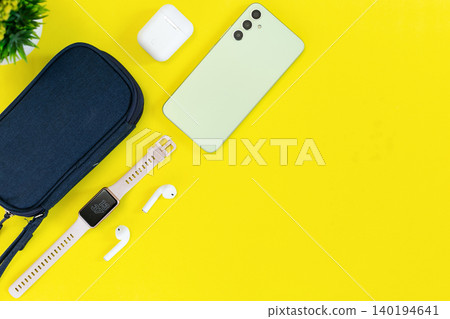 Minimalist tech setup on bright yellow background. Modern smartphone, smartwatch, earbuds, and case neatly arranged. Clean aesthetic suits lifestyle, wellness, or tech-focused content 140194641