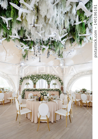 Elegant wedding reception hall featuring round tables, white and gold chairs, and floral arrangements Elegant wedding reception hall featuring round tables, white and gold chairs, and floral arrangements 140196191