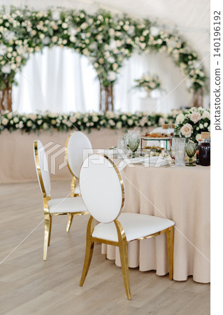 Elegant wedding reception hall featuring round tables, white and gold chairs, and floral arrangements Elegant wedding reception hall featuring round tables, white and gold chairs, and floral arrangements 140196192