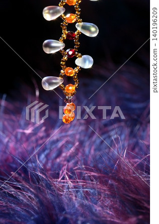 Orange jewel necklace over blue purple feather Orange jewel necklace over blue purple feather 140196209