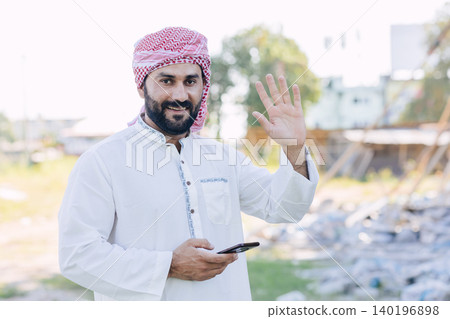 Happy smiling Saudi business man, Arab muslim adult male portrait standing hand waving hello Happy smiling Saudi business man, Arab muslim adult male portrait standing hand waving hello 140196898