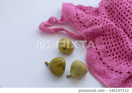 Green Figs Next to Pink Crochet Mesh Bag on White Background Green Figs Next to Pink Crochet Mesh Bag on White Background 140197212