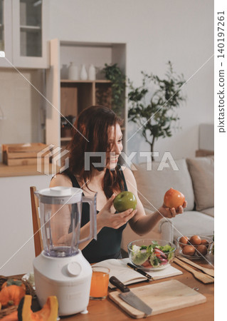 Woman preparing green smoothie in bright kitchen with fresh fruits and vegetables, healthy eating lifestyle moment in natural daylight Woman preparing green smoothie in bright kitchen with fresh fruits and vegetables, healthy eating lifestyle moment in natural daylight 140197261