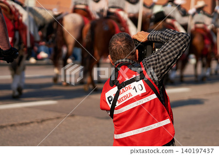 A media photographer in a red press vest taking pictures of a horse procession during the Calgary Stampede Parade. A media photographer in a red press vest taking pictures of a horse procession during the Calgary Stampede Parade. 140197437