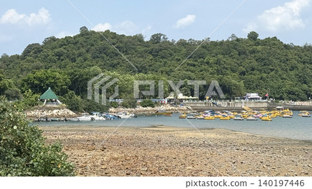 Scenic coastal view with a lush green hill, boats, and recreational watercraft Scenic coastal view with a lush green hill, boats, and recreational watercraft 140197446