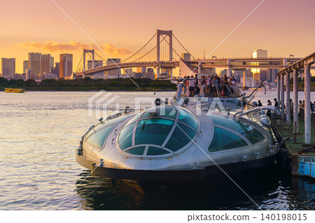 Tokyo, Japan - Oct 13 2024, panoramic view of Hotaluna water bus moored at the Odaiba Island marina in Tokyo Bay and loading passengers, rainbow bridge in the background, at evening, Tokyo, Japan Tokyo, Japan - Oct 13 2024, panoramic view of Hotaluna water bus moored at the Odaiba Island marina in Tokyo Bay and loading passengers, rainbow bridge in the background, at evening, Tokyo, Japan 140198015